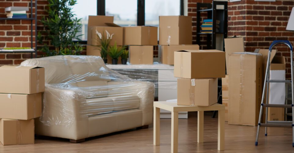 Office relocation - No people in empty living room apartment with carton boxes on stack, moving cardboard storage packaging in new household. Nobody in relocation property with interior furniture cargo.