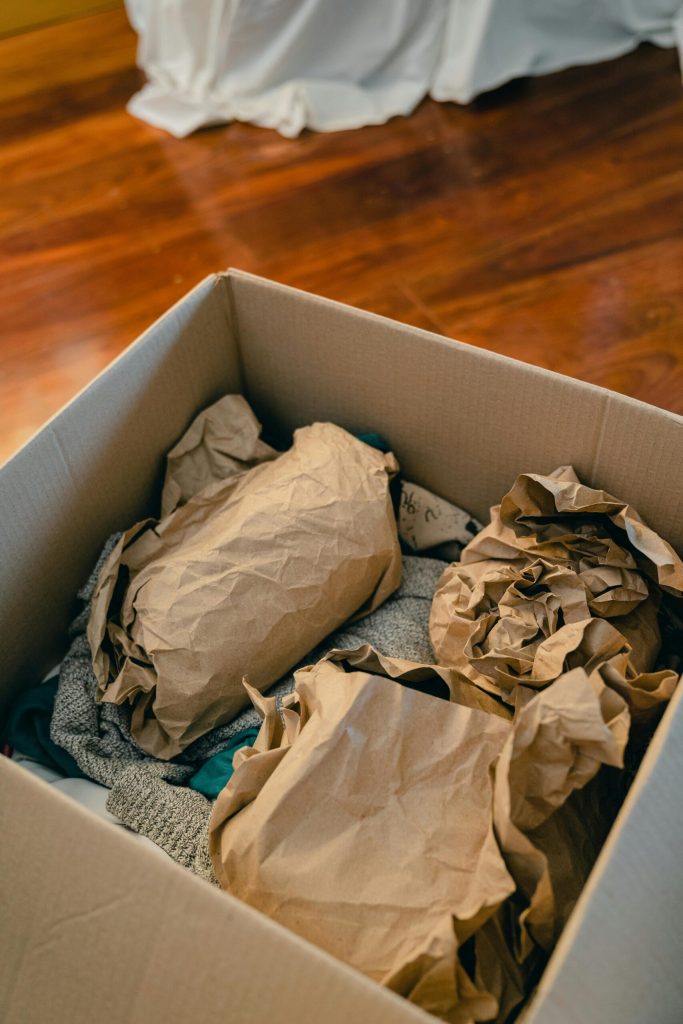 Best packers and movers within Mumbai - From above of open cardboard box on wooden floor full of things wrapped in packaging paper prepared for moving in new apartment